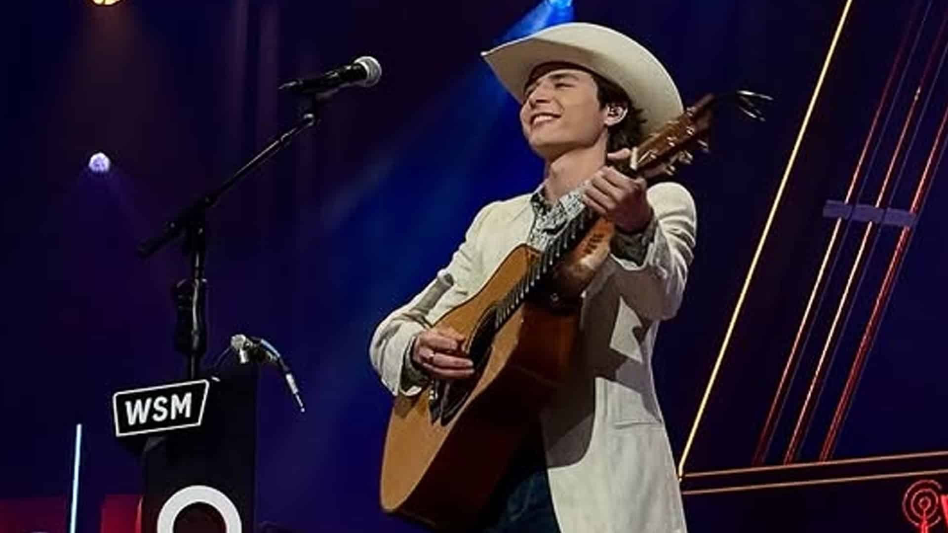 John Foster smiles while playing guitar during his Grand Ole Opry debut, opening with “Murder on Music Row” in a bold nod to traditional country music.