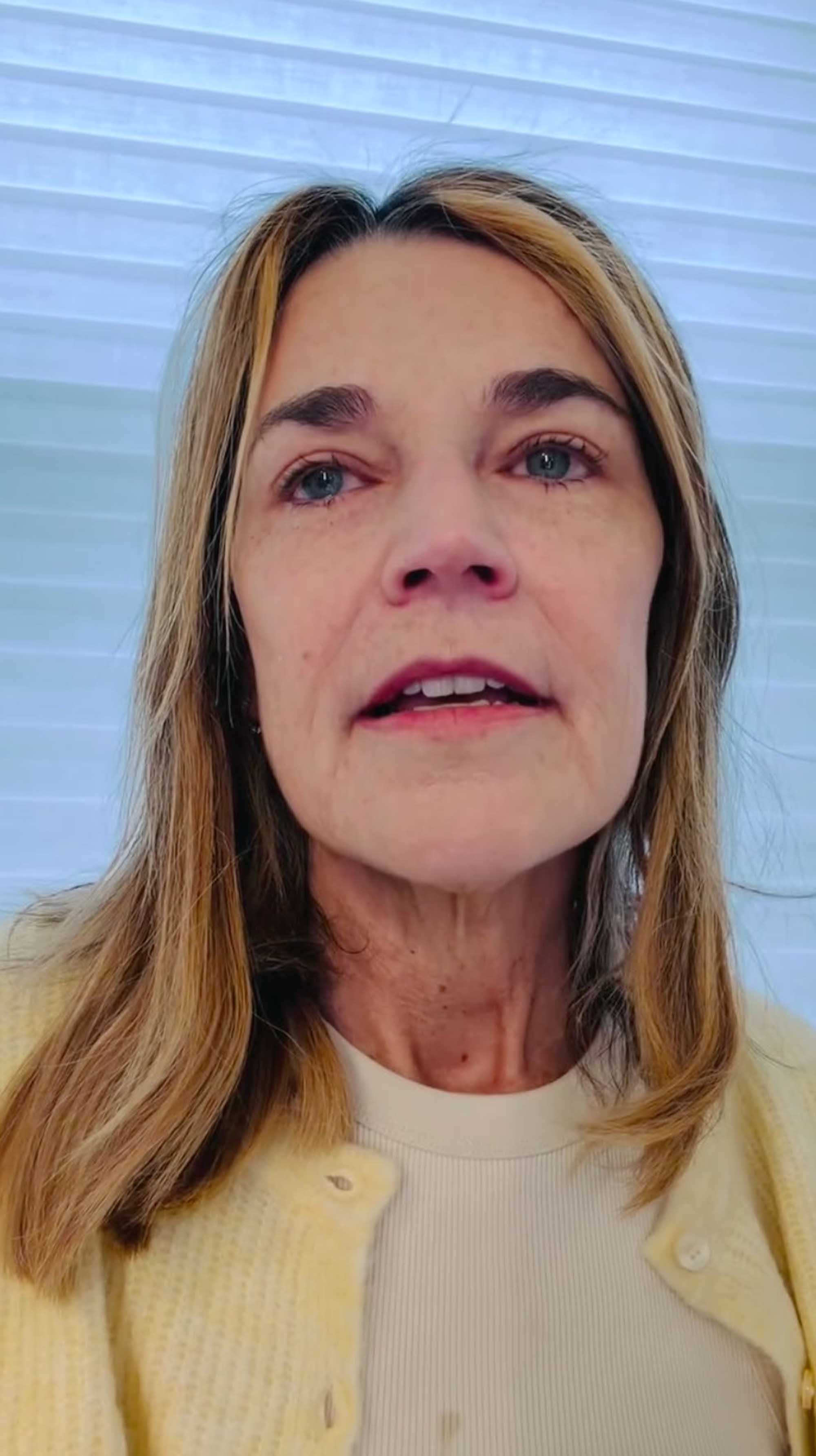 A light-skinned woman with blonde hair, wearing a white shirt and yellow cardigan, speaking to the camera.
